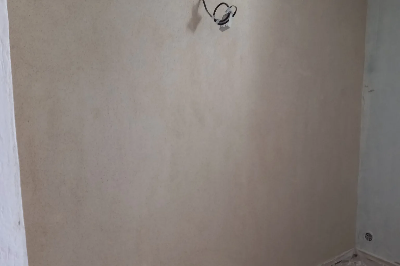 Plombier utilisant une caméra thermique pour localiser une fuite dans un mur taché d’humidité, avec mallette ouverte et détecteur de gaz à proximité, dans un intérieur moderne